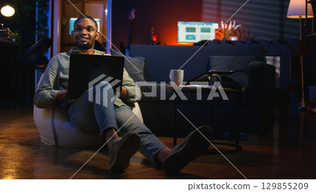 Guy checking financial balance and working on accounting analysis, ensuring company revenue growth at home. African american worker enjoys remote job using economy statistics. Camera A. Guy checking financial balance and working on accounting analysis, ensuring company revenue growth at home. African american worker enjoys remote job using economy statistics. Camera A. 129855209