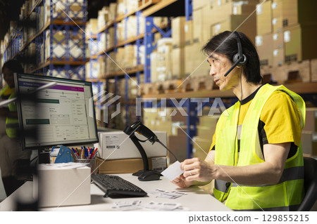 Call center employee assisting customers in a fulfillment center, handling inventory control and package tracking. Asian man resolving issues related to delivery delays or wrong addresses. Call center employee assisting customers in a fulfillment center, handling inventory control and package tracking. Asian man resolving issues related to delivery delays or wrong addresses. 129855215