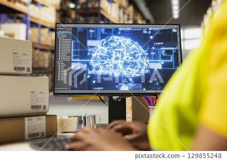 Black woman worker using AI neural network system to help with order processing, working in industrial warehouse with artificial intelligence. Parcel status monitoring for automation. 129855248