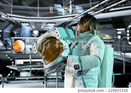 Astronaut holds helmet in orbital station, analyzing Mars planetary data on digital monitors. Crew member observes Martian surface research to assist future planetary exploration and mission planning 129855350