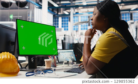 Black woman working in photovoltaics factory using copy space on PC to improve solar panels assembly processes. Assembly line engineer using mockup computer to calibrate equipment. Camera B. 129855362
