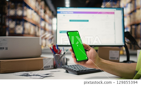 Warehouse staff in a hi-vis vest uses copy space display with technology of shipping software, packaging systems and inventory management tools. automation in e-commerce logistics. Camera A. 129855394