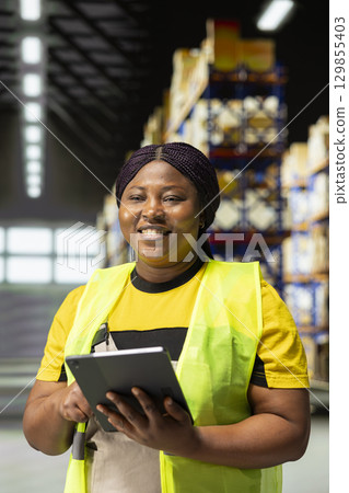 Worker wearing safety vest manages packages and process orders in compact distribution hub. This local shipping operation is in-house, supporting a growing e-commerce business. 129855403
