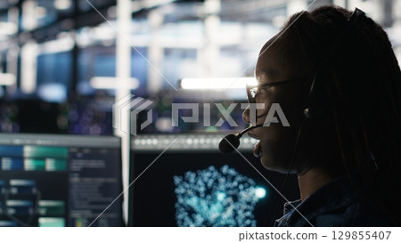 Data center employee uses audio headset and visual programming dashboard to troubleshoot client reported issues. Server farm technician looks at node tree interface, talking in microphone Data center employee uses audio headset and visual programming dashboard to troubleshoot client reported issues. Server farm technician looks at node tree interface, talking in microphone 129855407