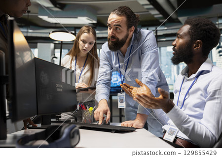 Team of programmers resolving critical error alert on screen in tech startup office, troubleshooting system warnings. IT staff members brainstorming fixes for office equipment failure 129855429