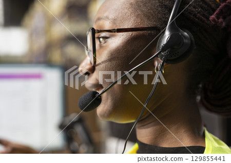 Close up of black woman answering calls from customers in a distribution hub, managing mix up problems and requests via customer support help line. Call center employee with headset. 129855441