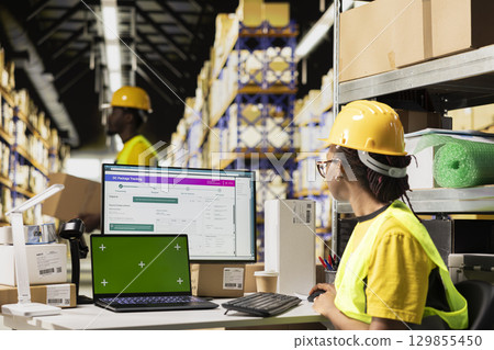 E-commerce worker registering airway bill numbers in the system with mockup, using shipping labels data for package tracking service. Using green screen in warehouse with storage racks. E-commerce worker registering airway bill numbers in the system with mockup, using shipping labels data for package tracking service. Using green screen in warehouse with storage racks. 129855450