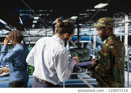 Army technicians using laptop to install server security systems in command center server farm. Military data center engineer and soldier overseeing computer networks for hybrid warfare. Army technicians using laptop to install server security systems in command center server farm. Military data center engineer and soldier overseeing computer networks for hybrid warfare. 129855516
