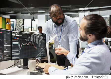 Manager supervising day trader in forex company office buying stocks to capitalize on market fluctuations. Prop firm team leader supervising tracking stock exchange price movements for profits 129855532