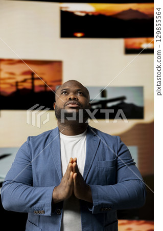 Black person with gratitude standing with hands together in prayer, radiating inner peace and strength for spiritual devotion. Man showcasing peace of mind and divine connection. 129855564
