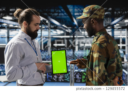 Diverse military base employees in data center use isolated mockup tablet to monitor defense systems via satellite surveillance. Army operators team ensuring government protection. 129855572