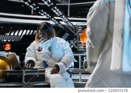 Female astronaut troubleshooting spacecraft hardware systems using laptop device. Woman in spaceship analyzing mission logs on notebook during planetary exploration flight 129855576