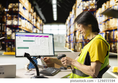 Asian male worker scanning shipment labels and tracking numbers in a distribution hub, ensures order management in fulfillment center. Using a scanner for transportation details. 129855594