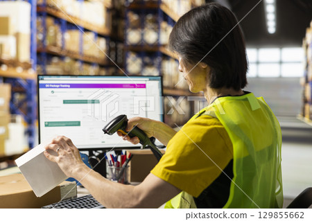 Fulfillment center staff engages in airway bills scanning for order tracking, using scanner on shipping labels in the warehouse. Worker wearing hi vis vest in storage room with shelves. Fulfillment center staff engages in airway bills scanning for order tracking, using scanner on shipping labels in the warehouse. Worker wearing hi vis vest in storage room with shelves. 129855662