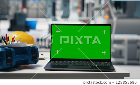 Empty desk and workspace with safety glasses and PC display setup in a solar energy facility, where robotic arms streamline the photovoltaic panel assembly process. Performance metrics. 129855686