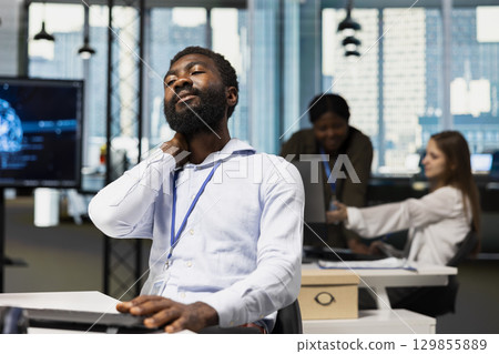 Tired system administrator at work relaxing stiff neck while using AI tools to automate routine coding tasks. Exhausted IT employee massaging neck to remove ache, using artificial intelligence Tired system administrator at work relaxing stiff neck while using AI tools to automate routine coding tasks. Exhausted IT employee massaging neck to remove ache, using artificial intelligence 129855889