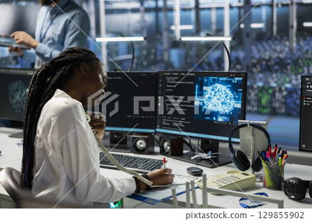 Female programmer in data center answers telephone call, assisting users with AI troubleshooting. Server room IT staff member talks in phone call, managing clients issues using artificial intelligence Female programmer in data center answers telephone call, assisting users with AI troubleshooting. Server room IT staff member talks in phone call, managing clients issues using artificial intelligence 129855902