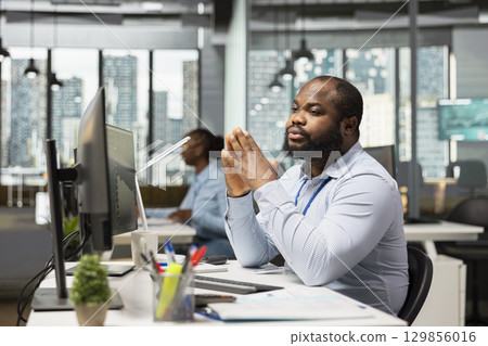 Trader in proprietary firm office monitoring stock exchange prices on multiple screens, trading securities. African american man using trading software to adjust hedge strategies during market swings Trader in proprietary firm office monitoring stock exchange prices on multiple screens, trading securities. African american man using trading software to adjust hedge strategies during market swings 129856016