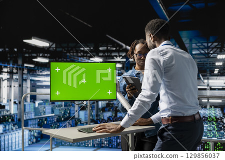 Black engineers monitoring neural network using green screen on pc, reviewing LLM visualization. Server farm IT experts oversee rigs powering machine learning processes, industrial platform. 129856037