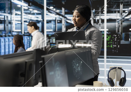 Software developer overseeing server clusters doing data intensive operations. IT expert using laptop to supervise supercomputers maintaining storage for machine learning 129856038