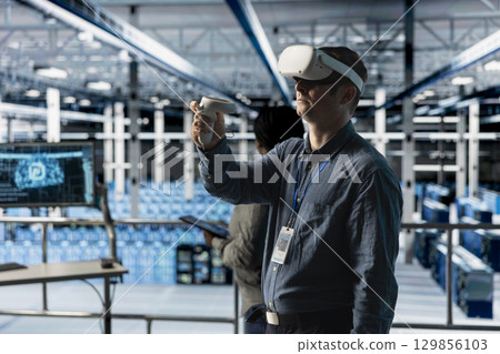 Server room worker simulating data center operations with VR headset and AI tech. Data center engineer using virtual reality technology and artificial intelligence to monitor server rigs Server room worker simulating data center operations with VR headset and AI tech. Data center engineer using virtual reality technology and artificial intelligence to monitor server rigs 129856103
