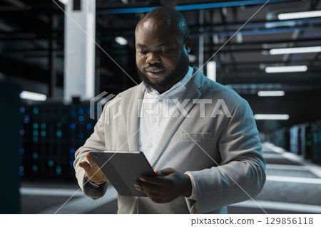 Engineer in server farm coordinating backups protocols, checking recovery plan. Data center IT specialist performing maintenance with tablet, making sure rigs are functioning optimally 129856118