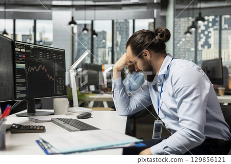 Upset day trader dejected after failing to capitalize on market fluctuations while buying and selling stocks. Frustrated man depressed in prop firm office after struggling to profit 129856121