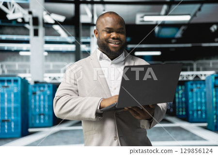 Happy programmer in server farm overseeing mainframes devices used for managing databases. Cheerful man in data center establishment doing checkup on rackmounts storing information Happy programmer in server farm overseeing mainframes devices used for managing databases. Cheerful man in data center establishment doing checkup on rackmounts storing information 129856124