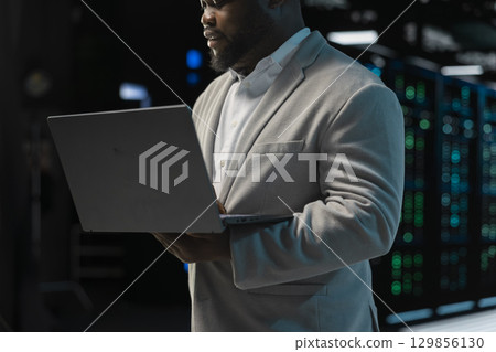 Close up of admin in server farm managing infrastructure systems, checking recovery plan on laptop. Data center IT expert monitoring performance, making sure mainframes are functioning optimally 129856130