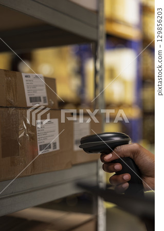 Close up of industrial depot worker scanning parcel details using tracking software, walking near huge storage racks. E-commerce delivery management system ensures accuracy in order processing. Close up of industrial depot worker scanning parcel details using tracking software, walking near huge storage racks. E-commerce delivery management system ensures accuracy in order processing. 129856203