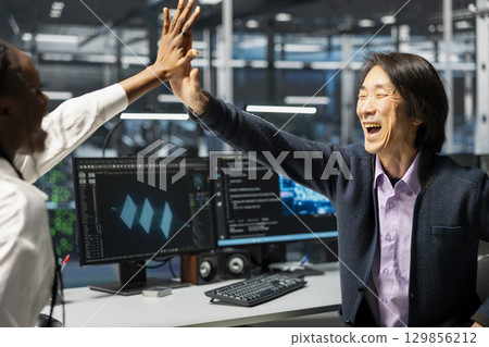 Overjoyed engineers in data center celebrate successfully installing server systems with AI. Delighted server hub workers doing high five, excited after upgrading gear using artificial intelligence 129856212