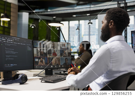 Tech company office coworkers working together via videocall, doing brainstorming on backup solutions to protect against data loss. African american man coding during online teleconference 129856255