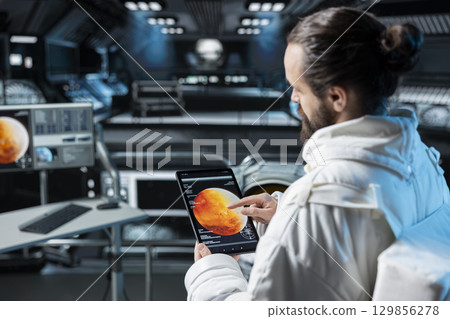 Astronaut using tablet to confirm suit integrity during journey to Mars. Orbital station crew member testing gear during routine equipment check during trip to red planet 129856278