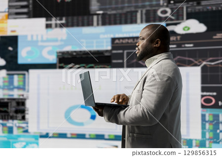African american businessman in a digital environment focused on graphs, working on strategic planning analysis for profitability and performance. Insightfulness and fintech forecasting. African american businessman in a digital environment focused on graphs, working on strategic planning analysis for profitability and performance. Insightfulness and fintech forecasting. 129856315
