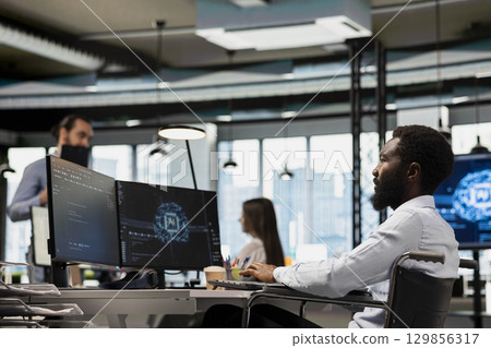 IT specialist in wheelchair developing software applications using AI automation. Programmer with paraplegia in inclusive office debugging applications with artificial intelligence IT specialist in wheelchair developing software applications using AI automation. Programmer with paraplegia in inclusive office debugging applications with artificial intelligence 129856317