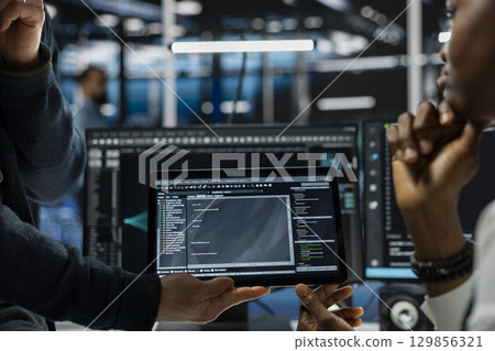 Close up of programmers coding on tablet in data center, refining algorithms for faster processing. IT workers using device in server room, conducting tests using software 129856321