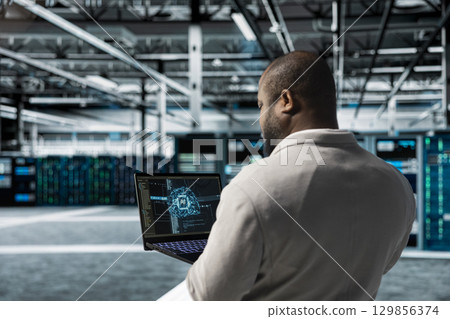 Admin using laptop in data center housing advanced equipment used for storing AI training datasets. Server room IT professional running artificial intelligence code to resolve technical issues 129856374