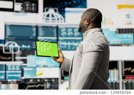 Young entrepreneur looks at tablet with chroma key for analysis, reviewing monthly reports and infographics for company development. Good performance metrics for growth, forecasting. Young entrepreneur looks at tablet with chroma key for analysis, reviewing monthly reports and infographics for company development. Good performance metrics for growth, forecasting. 129856384