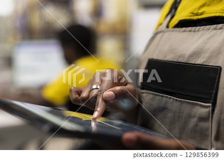 Close up of female employee ensuring awb tracking info within e-commerce inventory system on tablet, overseeing storage distribution protocols. Logistics planning for smooth cargo movement. 129856399