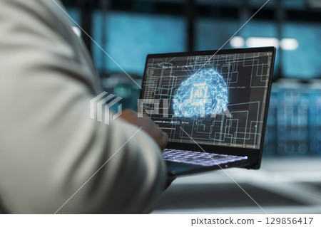 Close up of data center technician using artificial intelligence computerized model on laptop to oversee operations. Server farm IT expert working with AI machine learning algorithms on device Close up of data center technician using artificial intelligence computerized model on laptop to oversee operations. Server farm IT expert working with AI machine learning algorithms on device 129856417