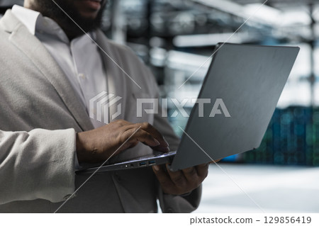Close up of data center worker running error checking utilities on laptop, automating anomaly detection. Server farm employee monitoring infrastructure performance, looking for network issues 129856419