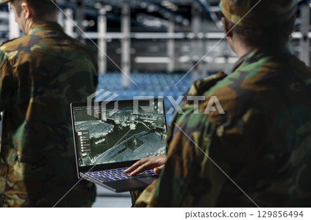 Close up of army specialist in data center scanning terrain after enemy lines using military satellite control. Soldier wearing uniform in server room managing orbital telemetry on notebook Close up of army specialist in data center scanning terrain after enemy lines using military satellite control. Soldier wearing uniform in server room managing orbital telemetry on notebook 129856494