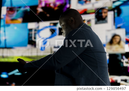 Black male person appears immersed in information overload, depicting the crisis and manipulation of social addiction. Dangerous social media dependence, mental health damage. Black male person appears immersed in information overload, depicting the crisis and manipulation of social addiction. Dangerous social media dependence, mental health damage. 129856497