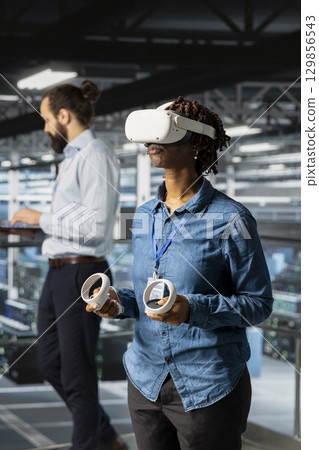 Woman engineer analyzing performance outputs using virtual reality tech on data center industrial platform. Server hub technician finetuning server rig configurations with VR headset. Woman engineer analyzing performance outputs using virtual reality tech on data center industrial platform. Server hub technician finetuning server rig configurations with VR headset. 129856543