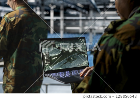 Close up of military technician in data center tracking satellite coordinates using laptop interface. IT specialist in server room analyzing reconnaissance data through satellite imaging systems Close up of military technician in data center tracking satellite coordinates using laptop interface. IT specialist in server room analyzing reconnaissance data through satellite imaging systems 129856548