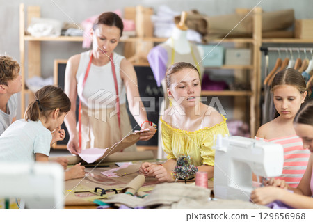 Sewing lesson - a group of teenage children learn to sew on sewing machine and cut fabric 129856968