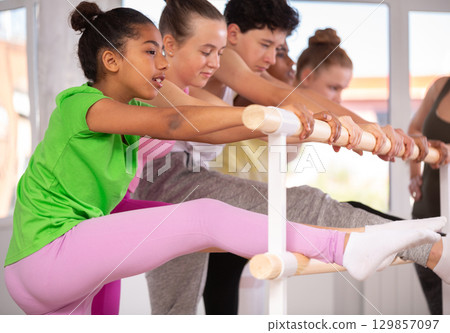 Dark-skinned teenage girl stretching at barre during beginner ballet class Dark-skinned teenage girl stretching at barre during beginner ballet class 129857097