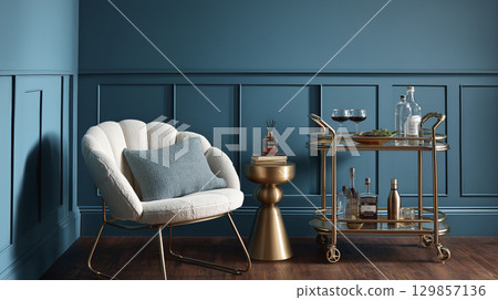 Luxurious modern interior design shows comfortable armchair beside striking blue wall. Elegant gold furniture, including stylish bar cart, decorates chic room, providing sophisticated and inviting 129857136