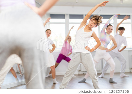 Male boy student repeats movements of unrecognizable teacher during group modern dance class. Male boy student repeats movements of unrecognizable teacher during group modern dance class. 129857306