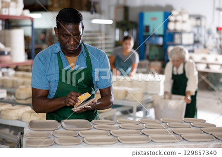 African american man using foam sponge smooths out roughness and irregularities on freshly made pottery 129857340